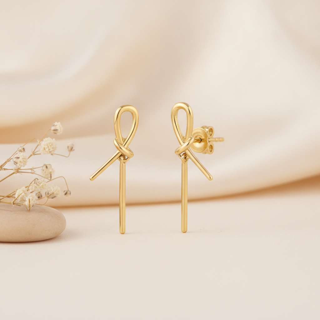 gold knot stud earrings with cascading linear drops, styled on a cream background with draped silk and dried flowers