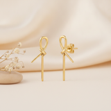 gold knot stud earrings with cascading linear drops, styled on a cream background with draped silk and dried flowers