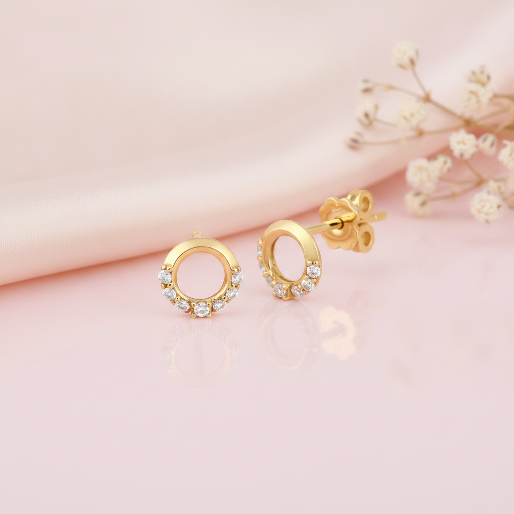 open circle gold stud earrings with clear stones along the lower edge, styled on a pink background with draped silk and dried flowers