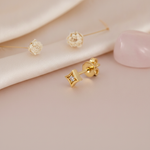 small gold star-shaped stud earring with a single clear stone, styled on a pink background with dried flower puffs and a pink stone