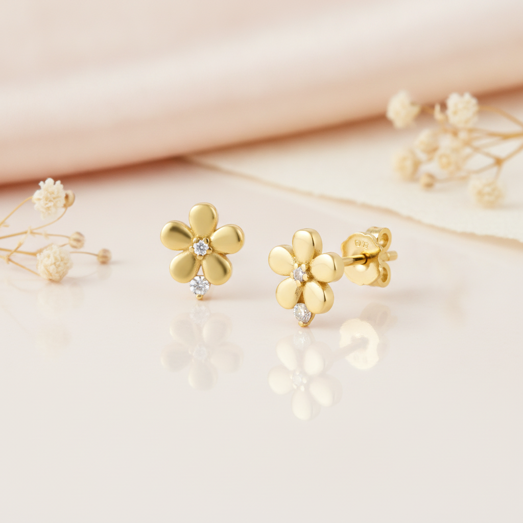 gold flower stud earrings with a clear stone center and a second stone at the base, styled on a pink background with draped silk and dried flowers