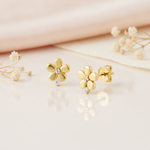 gold flower stud earrings with a clear stone center and a second stone at the base, styled on a pink background with draped silk and dried flowers