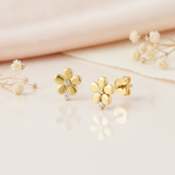 gold flower stud earrings with a clear stone center and a second stone at the base, styled on a pink background with draped silk and dried flowers