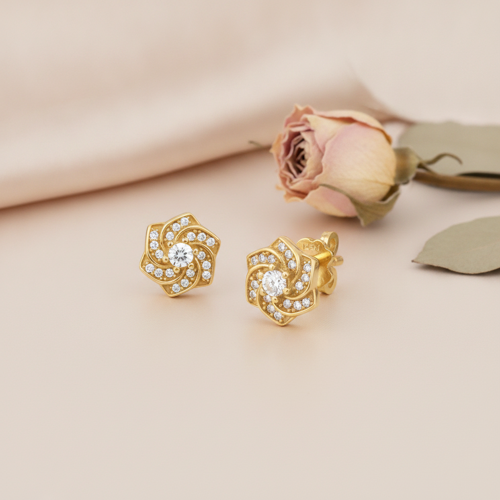 swirling gold rosette stud earrings with pave clear stones and a round center stone, styled on a cream background with a dried rose and leaf