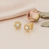 swirling gold rosette stud earrings with pave clear stones and a round center stone, styled on a cream background with a dried rose and leaf