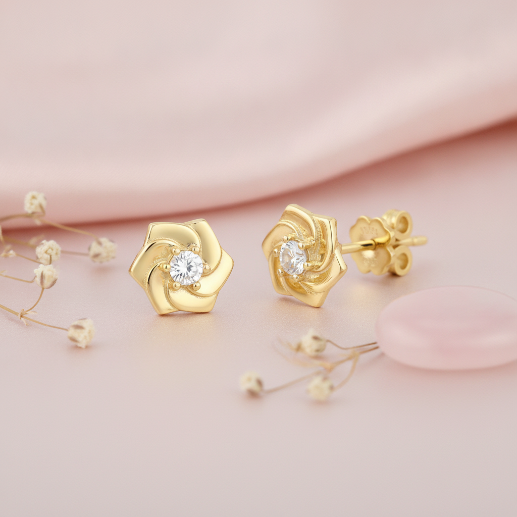 spiraling gold pinwheel stud earrings with a single clear center stone, styled on a pink background with dried flowers and a pink stone