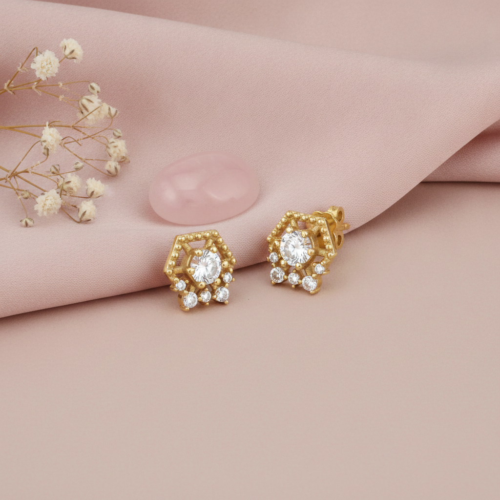 beaded hexagonal gold stud earrings with a clear center stone and White CZ accents, styled on a pink background with dried flowers and a pink stone