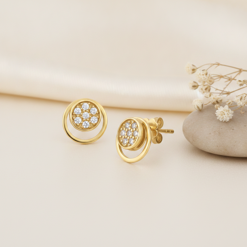 open gold circle stud earrings with a pave cluster of clear stones at center, styled on a cream background with draped silk and a stone