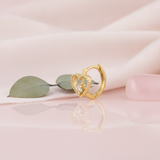 beaded open heart gold huggie hoop earring with a single clear stone, styled on a pink background with eucalyptus leaves and a pink stone