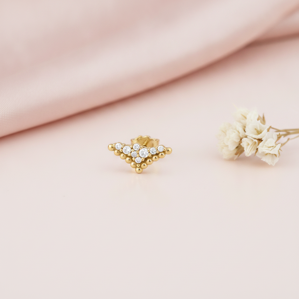 tapered chevron gold stud earrings with a cluster of clear stones, styled on a pink background with dried baby's breath flowers