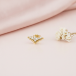 tapered chevron gold stud earrings with a cluster of clear stones, styled on a pink background with dried baby's breath flowers
