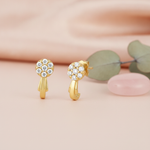 gold cluster hoop earrings with White CZ stones and a curved sweeping band, styled with eucalyptus leaves and a pink stone on a pink background