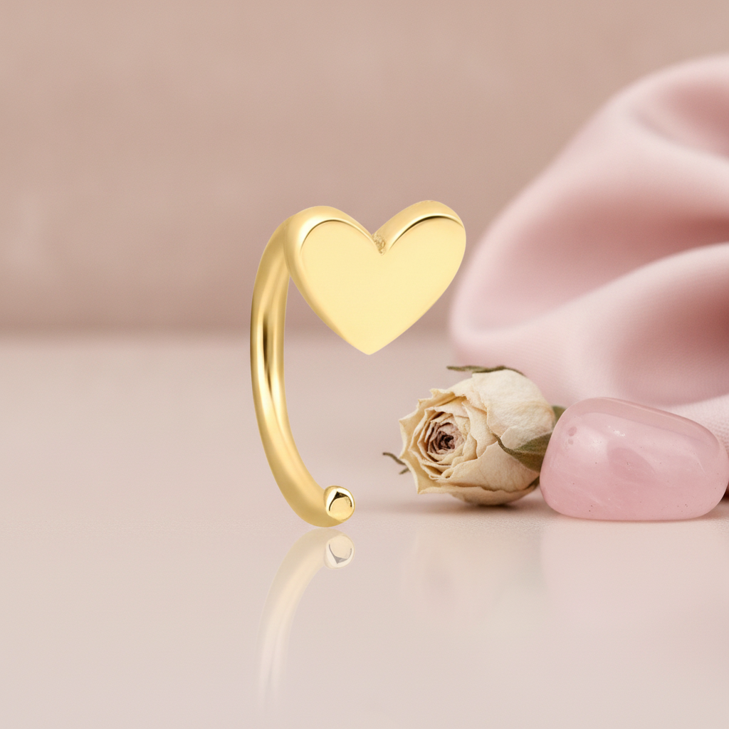 gold heart charm on an open curved hoop earring, styled with a dried rose and a pink stone on a blush background