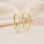gold double hoop earrings with a dangling clear round stone, styled with a dried flower and a pink stone on a blush background
