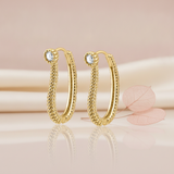 gold beaded oval hoop earrings with a White CZ stone accent, styled with a dried leaf on a blush background