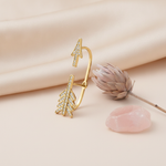 gold split arrow ear cuff earring with pave White CZ stones, styled with a dried flower and a pink stone on a cream background
