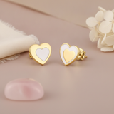 gold heart stud earrings with a white inlay center, styled with white flowers and a pink stone on a mauve background