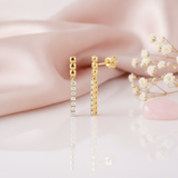 gold beaded drop earrings with a linear row of White CZ stones, styled with baby's breath flowers and a pink stone on a pink background