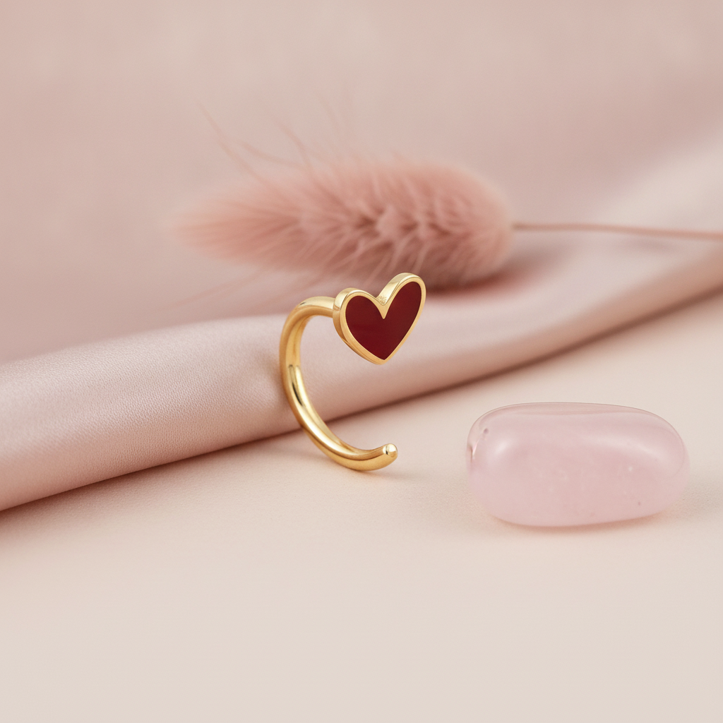 gold open curve earring with a red enamel heart accent, styled with a dried pink flower and a rose quartz stone on a blush background