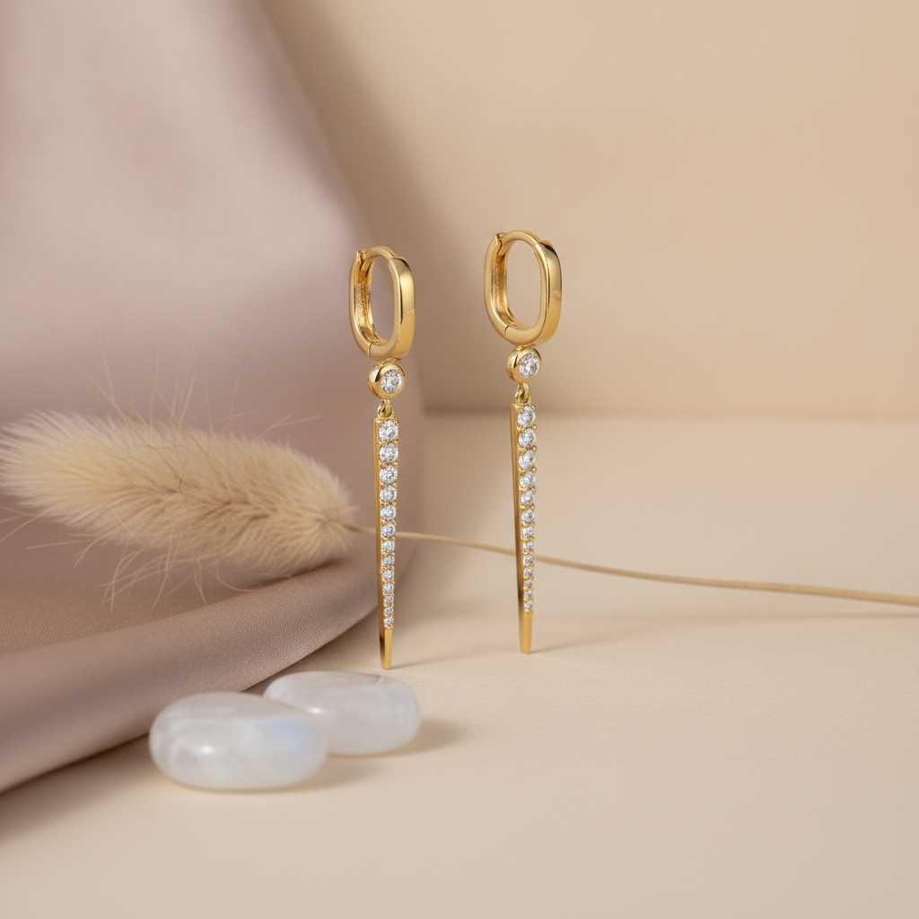 gold huggie hoop earrings with a tapered pave spike drop, styled with a dried flower and moonstone beads on a beige background