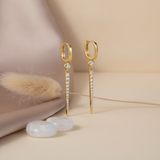 gold huggie hoop earrings with a tapered pave spike drop, styled with a dried flower and moonstone beads on a beige background