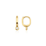 yellow gold oval huggie earrings with a bezel-set clear stone on white background