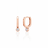 rose gold oval huggie earrings with a bezel-set clear stone on white background