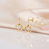 gold circle drop earrings with a pave heart charm, styled with dried flowers and a rose quartz stone on a blush background with mirrored reflection