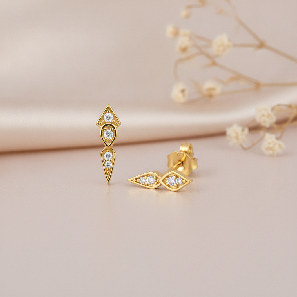 gold tapered stud earrings with stacked kite and teardrop frames set with clear stones, on a blush silk background with dried baby's breath