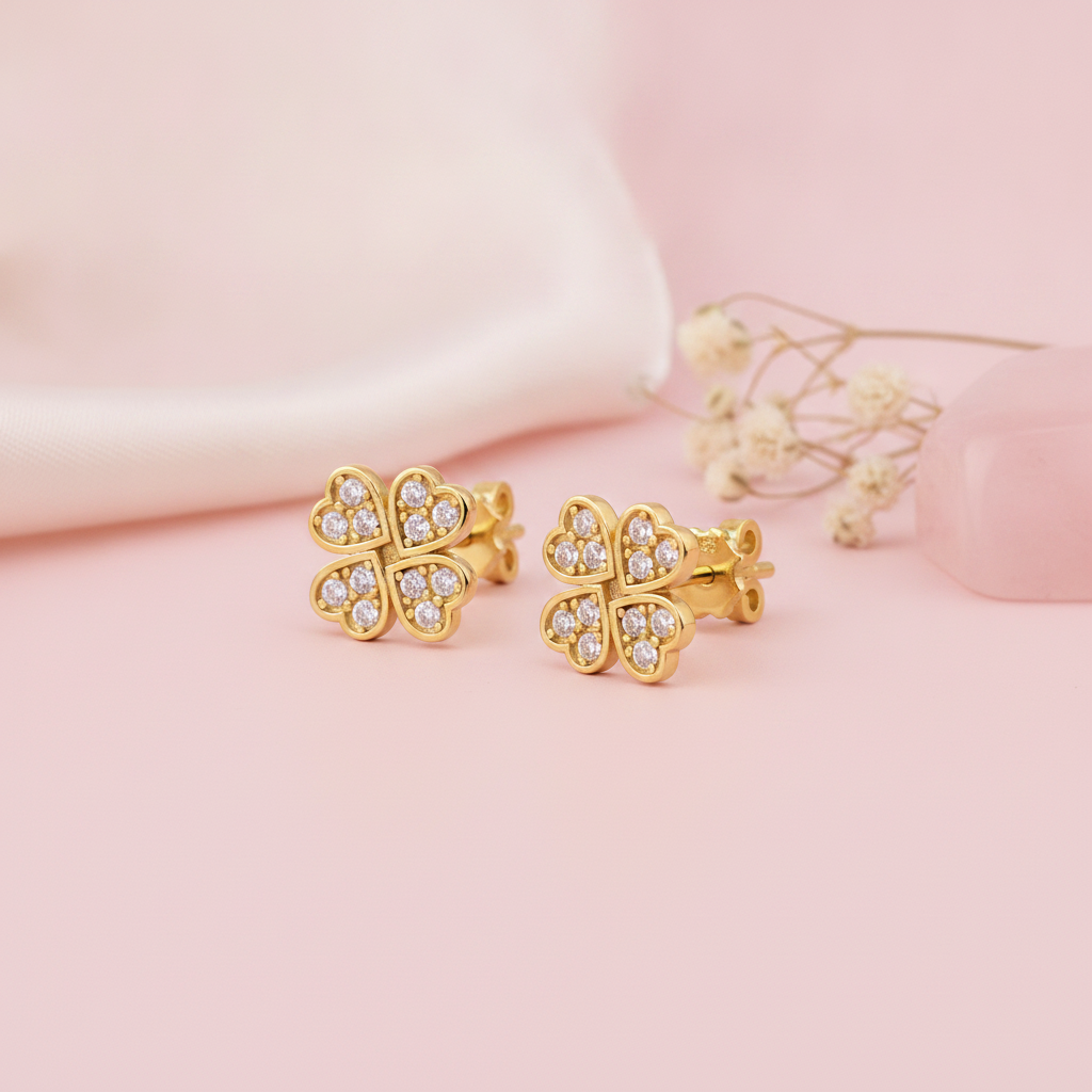 gold four-leaf clover stud earrings with clear pave stones on a pink background with dried baby's breath