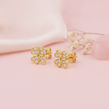 gold four-leaf clover stud earrings with clear pave stones on a pink background with dried baby's breath