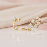 gold open hoop earrings topped with a cluster of clear stones, styled with dried baby's breath on a blush background