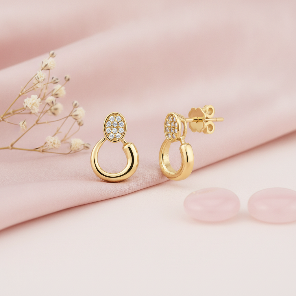 gold oval pave stud earrings descending into an open loop, styled with dried baby's breath and pale pink stones on a blush background