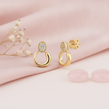 gold oval pave stud earrings descending into an open loop, styled with dried baby's breath and pale pink stones on a blush background