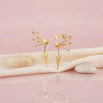 gold sculptural earrings with curved pave bands, a faceted pyramid center and a sharp spike, styled with dried grasses on a pink background