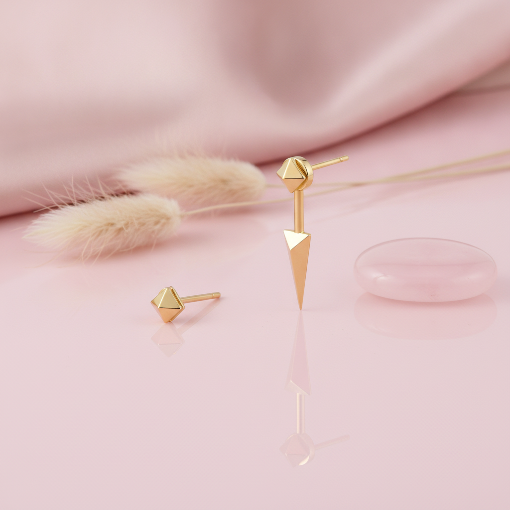 gold faceted pyramid stud earring and a pyramid-topped spike drop stud earring on a pink background with dried grass