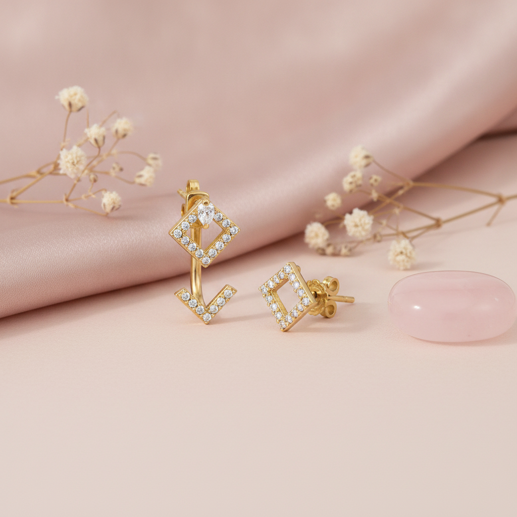 gold rhombus stud earrings with a pear-cut stone and floating chevron jacket, styled on a blush fabric backdrop with dried flowers and a pink stone