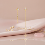 asymmetrical gold starburst drop earrings on chains of different lengths styled on a blush fabric backdrop with dried flowers and a pink stone