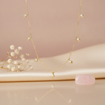 gold necklace with V-shaped chevron drops set with White CZ stones styled on a blush fabric backdrop with dried flowers and a pink stone