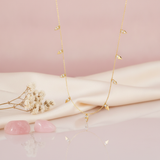gold necklace with small triangular charms alternating polished gold and pave stones styled on a blush and cream fabric backdrop with dried flowers and pink stones
