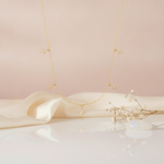 gold necklace with starburst charms and a center compass star pendant styled on a cream fabric backdrop with dried flowers and a moonstone