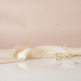 gold necklace with starburst charms and a center compass star pendant styled on a cream fabric backdrop with dried flowers and a moonstone