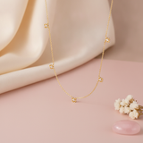gold necklace with four-petal flower stations and White CZ center stones styled on a blush and cream fabric backdrop with dried flowers and a pink stone