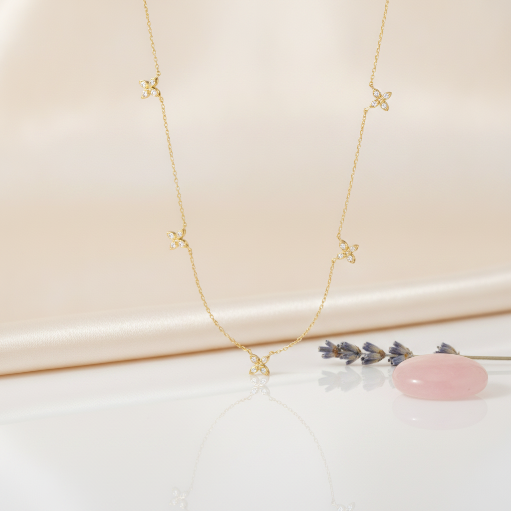 gold floral station necklace styled with a pink stone and dried lavender on a blush background