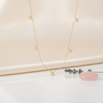 gold floral station necklace styled with a pink stone and dried lavender on a blush background