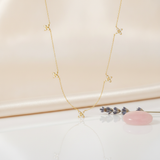 gold floral station necklace styled with a pink stone and dried lavender on a blush background