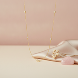 gold necklace with scattered bezel-set stones styled with dried flowers and a pink stone on a blush background