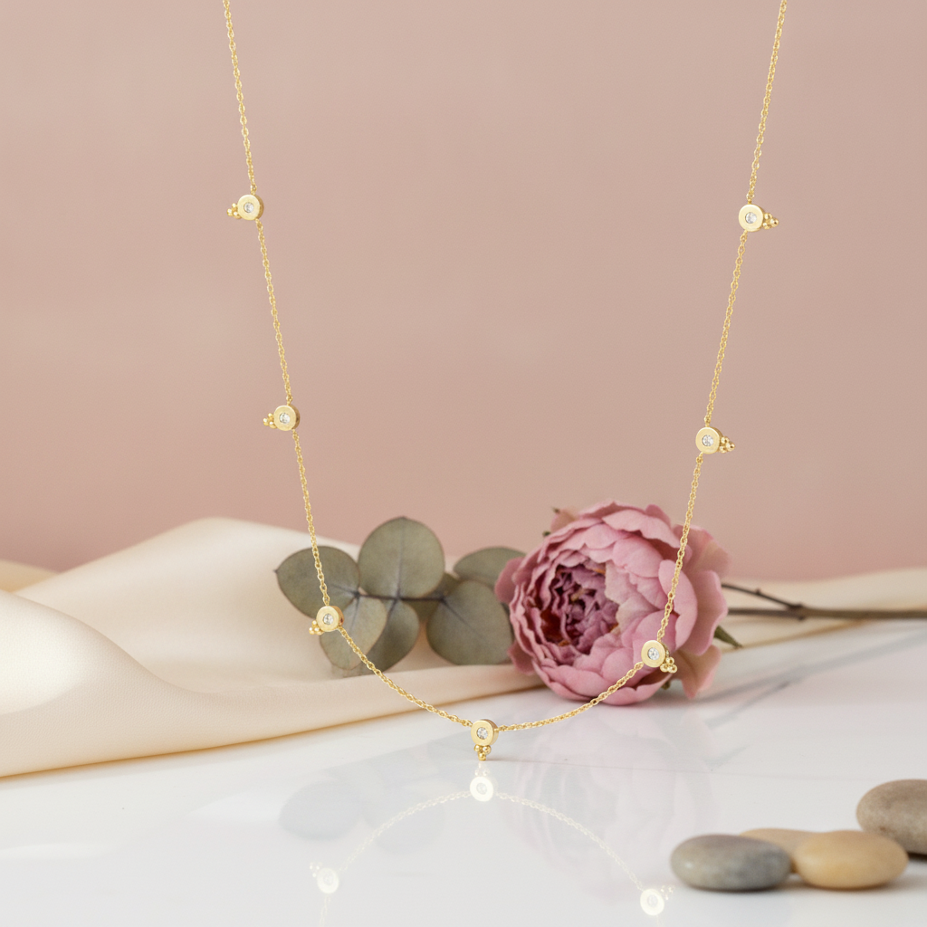 gold necklace with bezel-set stone stations styled with a pink peony and eucalyptus on a blush background
