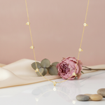 gold necklace with bezel-set stone stations styled with a pink peony and eucalyptus on a blush background