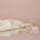 gold pave hoop pendant necklace styled with dried baby's breath and a pink stone on a blush background
